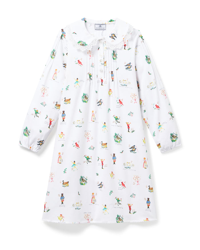 The Girl's Twill Lola Nightgown in 12 Days of Christmas is a white long-sleeve children’s dress with a Peter Pan collar and a playful pattern of colorful people, animals, and plants scattered across the fabric.