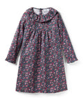 The Girl's Twill Scarlett Nightgown in Fleurs de Saison is a long-sleeved, knee-length dress with a ruffled collar and cuffs, featuring pink and white flowers with green leaves on a dark background.