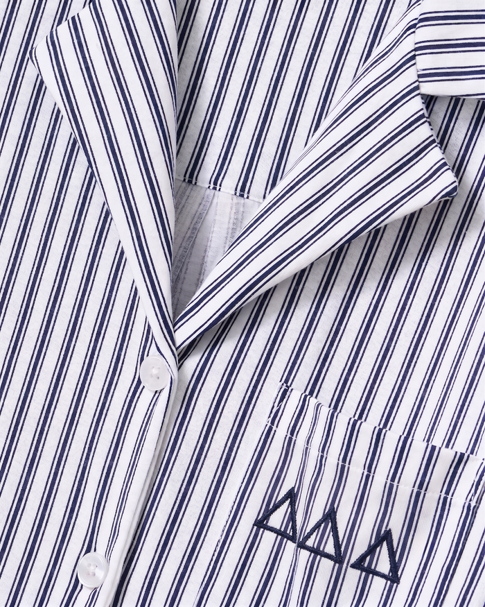 Close-up of the Greek Embroidered Olivia Pima Short Set in Navy French Ticking, featuring a white shirt with thin black vertical stripes, white buttons, and a small pocket adorned with three embroidered black triangles.