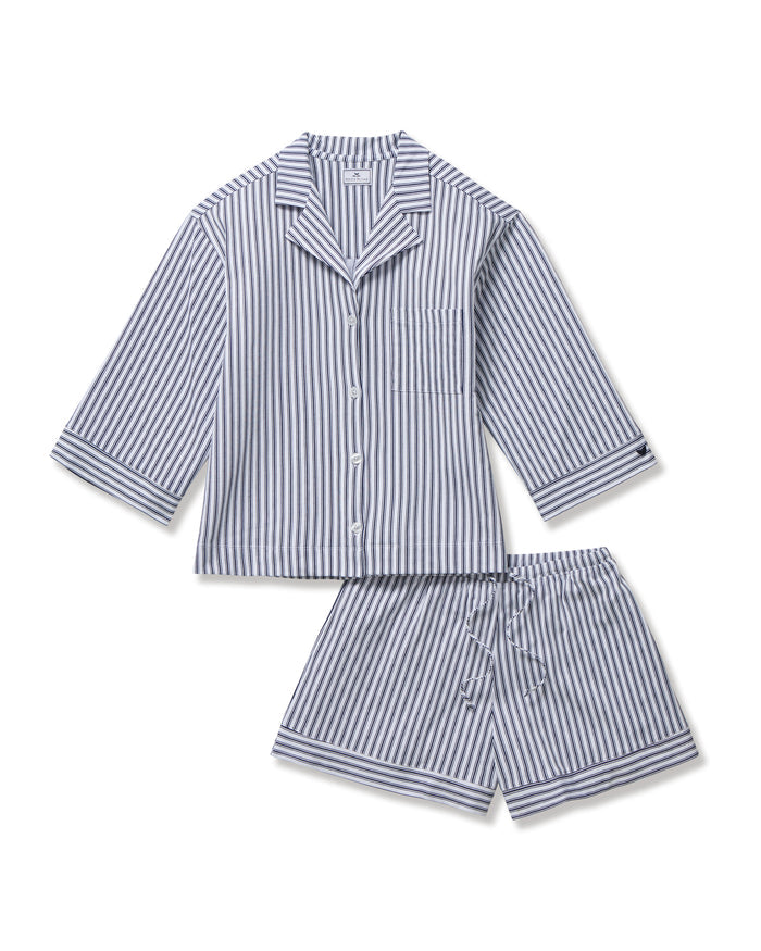 The Olivia Pima Short Set in Navy French Ticking features a matching set of blue and white vertical striped pajamas with a long-sleeve, button-up shirt with chest pocket and drawstring shorts.