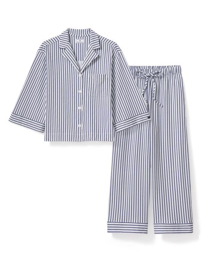 A person with long dark hair is wearing Petite Plumes Olivia Wide Leg Pima Pajama Set in Navy French Ticking, crafted from luxurious Peruvian Pima cotton. The button-up shirt and wide-legged pants have vertical stripes in alternating dark and light colors. They stand barefoot against a plain background.