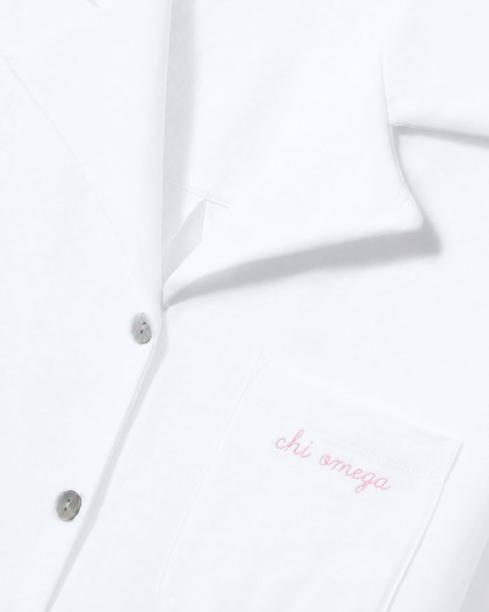 Greek Embroidered Olivia Pima Short Set in White, featuring a button-up shirt with a close-up of the collar and pocket. The pocket is embroidered with “chi omega” in light pink cursive text.