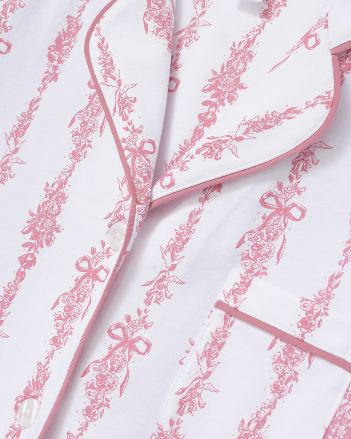 Close-up of The Poppy Pima Short Set in Pink Mayfair Toile, featuring a white pajama shirt adorned with pink floral and bow patterns, pink piping along the collar and pocket, and finished with white buttons.