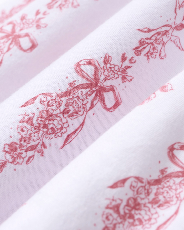 Close-up of the Poppy Pima Short Set in Pink Mayfair Toile, showcasing white fabric adorned with a repeating pink floral toile pattern featuring bouquets tied with ribbon bows and delicate leaves.
