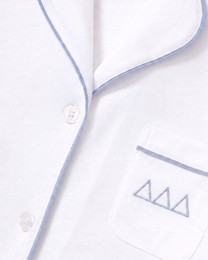 Close-up of the Greek Embroidered Poppy Pima Short Set pajama top in white with periwinkle piping, featuring three buttons and a pocket adorned with three small blue embroidered triangle designs above the trim.