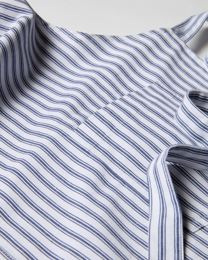 Close-up of the Kids Apron in Navy French Ticking by Petite Plume, featuring blue and white vertical stripes. The fabric is draped with slight wrinkles, producing varying shades and highlights. Perfect for children.