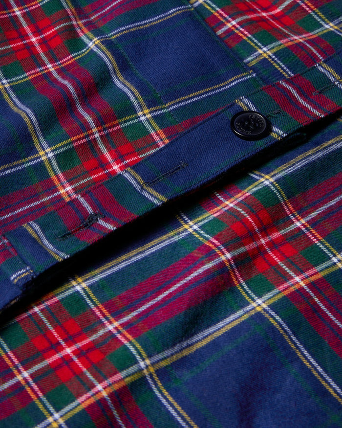 Close-up of the Kids Apron in Windsor Tartan by Petite Plume, featuring a festive plaid pattern of red, green, blue, and white stripes with a central black button—ideal for holiday baking.