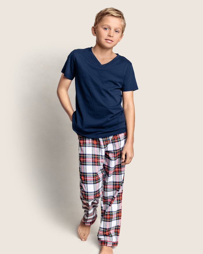 A young boy with short blond hair wears a navy blue T-shirt and Petite Plumes Kids Brushed Cotton Pajama Pant in Balmoral Tartan. He stands with one hand in his pocket against a plain light-colored background.