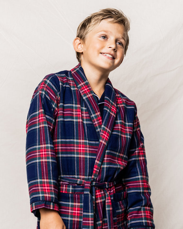 A smiling young boy wearing the Kid’s Brushed Twill Robe in Windsor Tartan stands against a light, plain background.