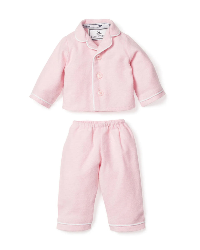 A person in a long-sleeved white shirt holds an adorable 18 baby doll with a light skin tone, dressed in Petite Plumes Kids Flannel Doll Pajamas in Pink, perfectly matching their own attire. Only the shoulder and one arm of the individual are visible.