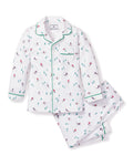 Petite Plumes Kids Flannel Pajama Set in Après Ski features a white skiing pattern with small figures and trees. The button-down top has green piping on the collar and cuffs, while the matching pants have an elastic waistband. Made from flame-retardant fabric for added safety and comfort.