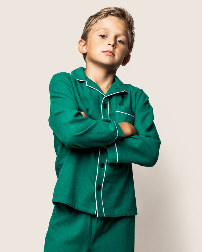 A confident young boy showcases the stylish Kids Flannel Pajama Set in Forest Green by Petite Plume, complete with white piping, against a neutral background.