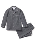 The Kids Flannel Pajama Set in Grey by Petite Plume offers a cozy design with white piping, featuring a button-up top with a chest pocket and pants with an elastic waistband. Made from soft, flame-retardant fabric, it ensures both comfort and safety.