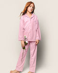 A young girl with long red hair stands in Petite Plumes Kids Flannel Pajama Set in Pink, holding a white flower against a plain, light-colored background.
