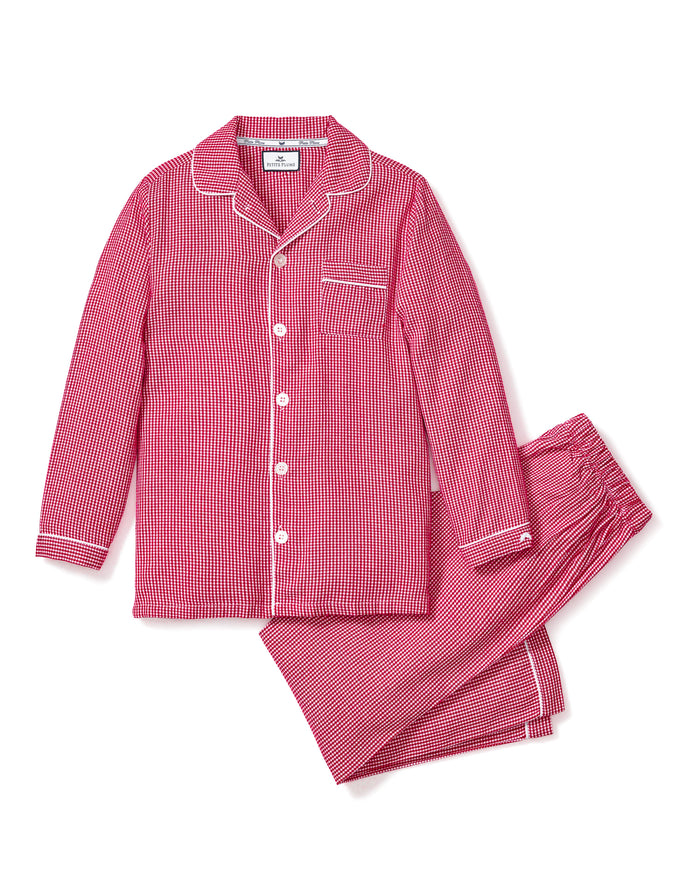 The Kids Flannel Pajama Set in Red Mini Gingham by Petite Plume offers luxurious sleepwear with a classic design, featuring red and white gingham. The set includes a long-sleeved button-up shirt with a chest pocket and matching pants with an elastic waistband for added comfort.
