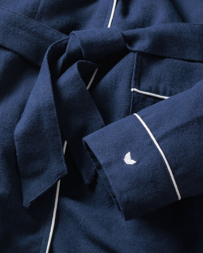 Close-up of Petite Plumes Kids Flannel Robe in navy with white piping, showcasing a tied belt and an embroidered crescent moon on the sleeve. The soft flannel fabric mimics pajamas or childrens sleepwear, providing comfort and style.