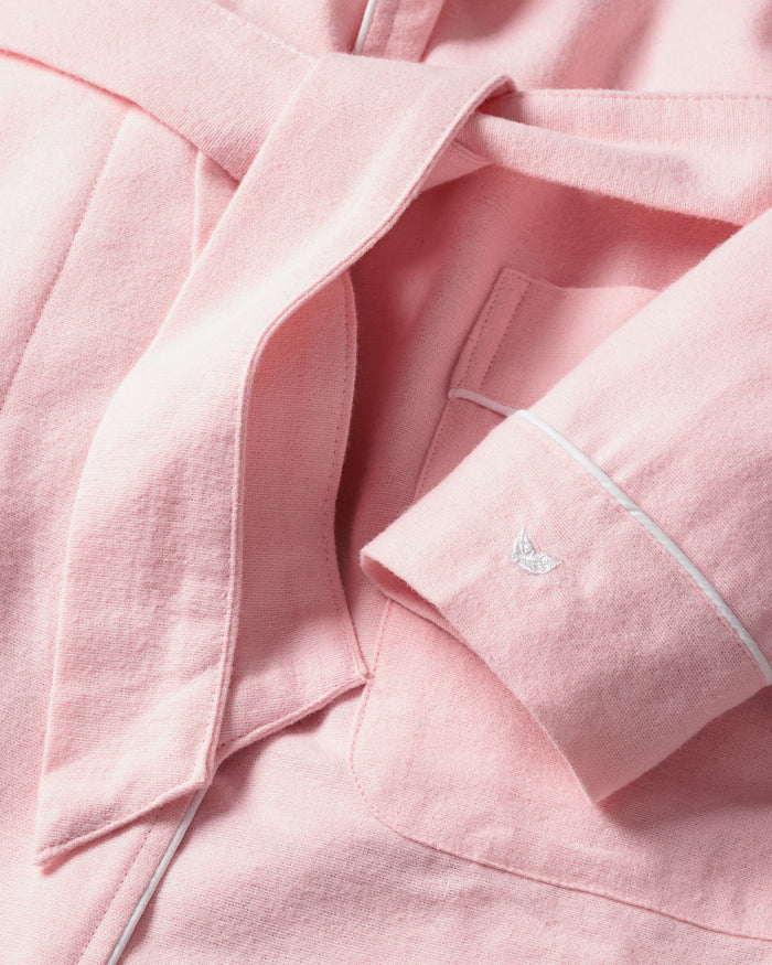 Close-up of Petite Plumes Kids Flannel Robe in Pink: a soft, chemical-free childrens sleepwear with a tie belt, pocket, and white-piped cuffs featuring an embroidered bird. The fabric is smooth yet slightly textured.