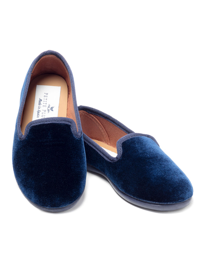 The Kids Hamptons Loafer in Navy Velvet by Petite Plume features a soft texture, rounded toes, tan inner lining with a label, and a sleek design. These Spanish-made slippers are elegantly displayed against a plain white background.