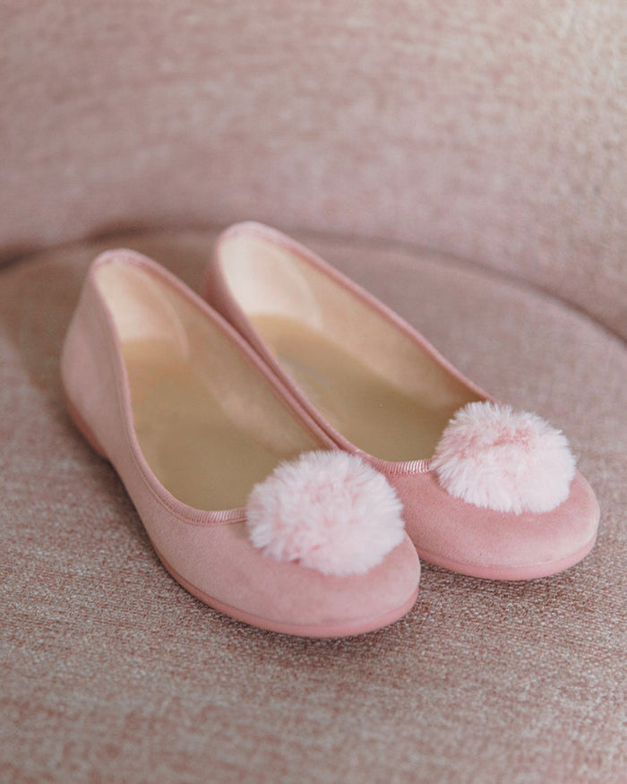 The Kids Juliette Slipper by Petite Plume in antique rose suede features festive pom-poms on the toes, set against a matching pink textured surface.