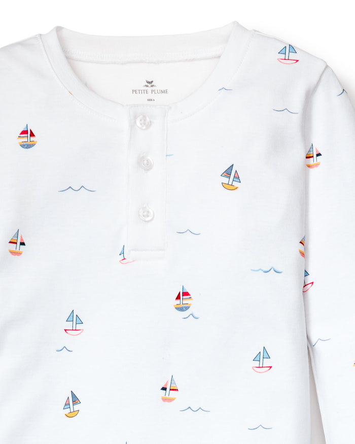 A close-up of the Kids Pima Snug Fit Pajama Set in Bateau by Petite Plume features a buttoned collar with vibrant, colorful sailboats and blue waves print.
