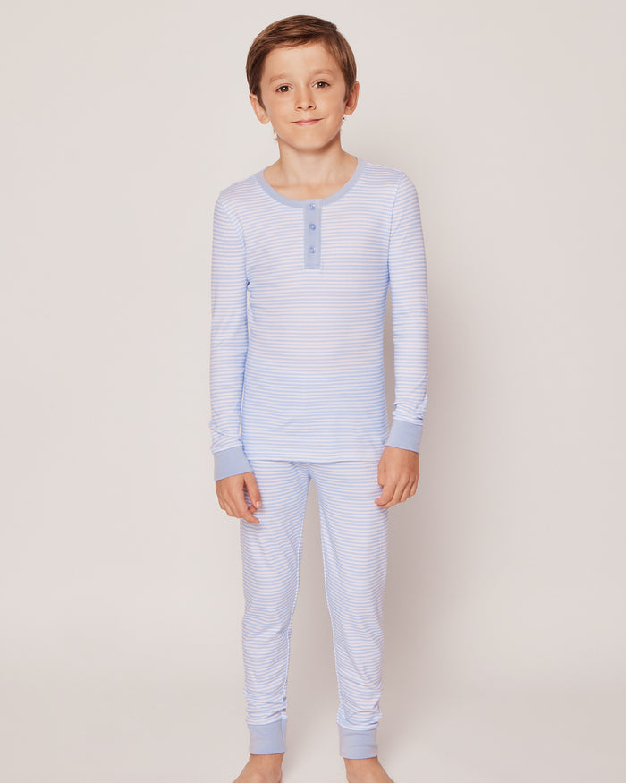 A young boy stands barefoot against a light background, wearing the Kids Pima Snug Fit Pajama Set in Blue Stripes by Petite Plume. His short brown hair complements his serene expression as he looks forward with a slight smile.