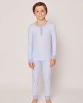 A young boy stands barefoot against a light background, wearing the Kids Pima Snug Fit Pajama Set in Blue Stripes by Petite Plume. His short brown hair complements his serene expression as he looks forward with a slight smile.