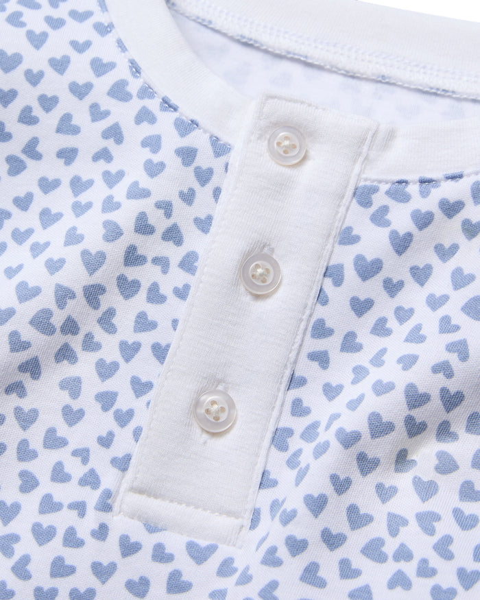 A close-up of the Kids Pima Snug Fit Pajama Set in Bluehearts by Petite Plume features a soft Pima Cotton white shirt with light blue heart patterns and a henley neckline with three white buttons, embodying coordinated style.