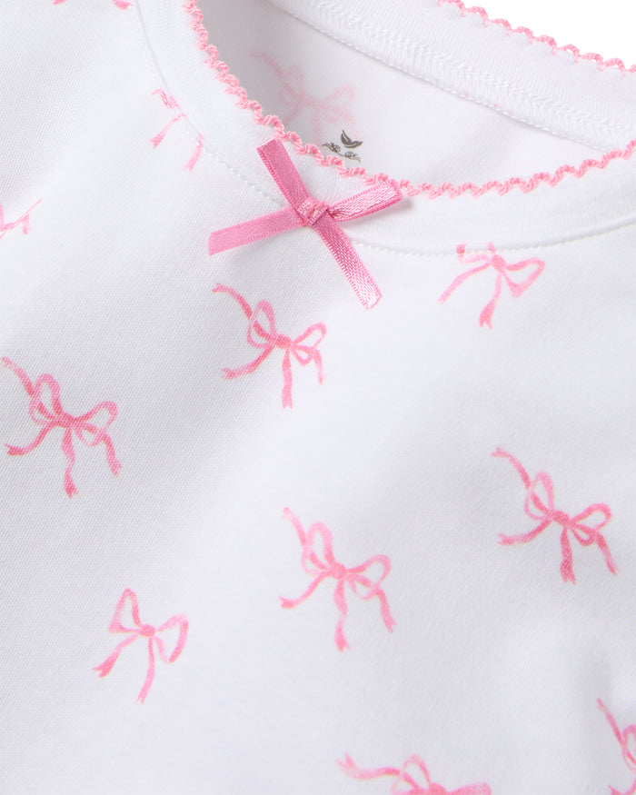 The Kid’s Pima Snug Fit Pajama Set in Blushing Bows by Petite Plume features a white shirt with pink bows, crafted from soft Pima cotton for ultimate comfort and sweet dreams.