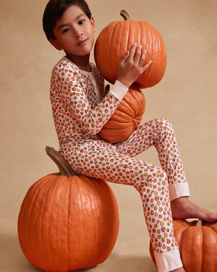 The Kids Pima Snug Fit Pajama Set in Pumpkin Patch by Petite Plume features a soft Pima Cotton long-sleeve top and pants. With a white background adorned with small colorful pumpkins, and solid white cuffs and neckline, this sleepwear set is charming and cozy for children.
