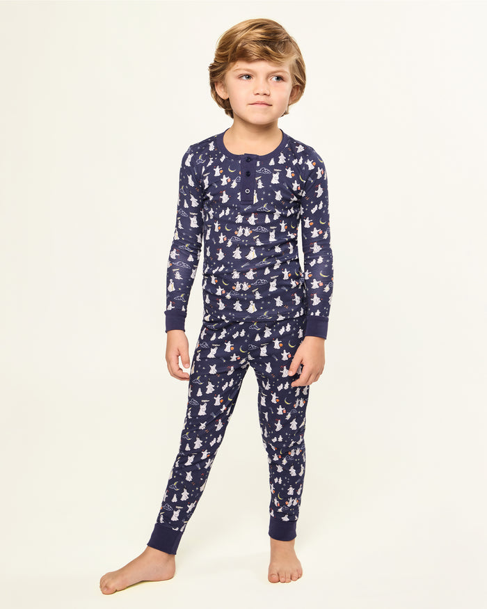 The Kid's Pima Snug Fit Pajama Set in Spooky Slumber is a navy blue pajama set with long sleeves and pants, featuring white and red cartoon dogs in winter gear, plus dark blue cuffs and button details on the top.