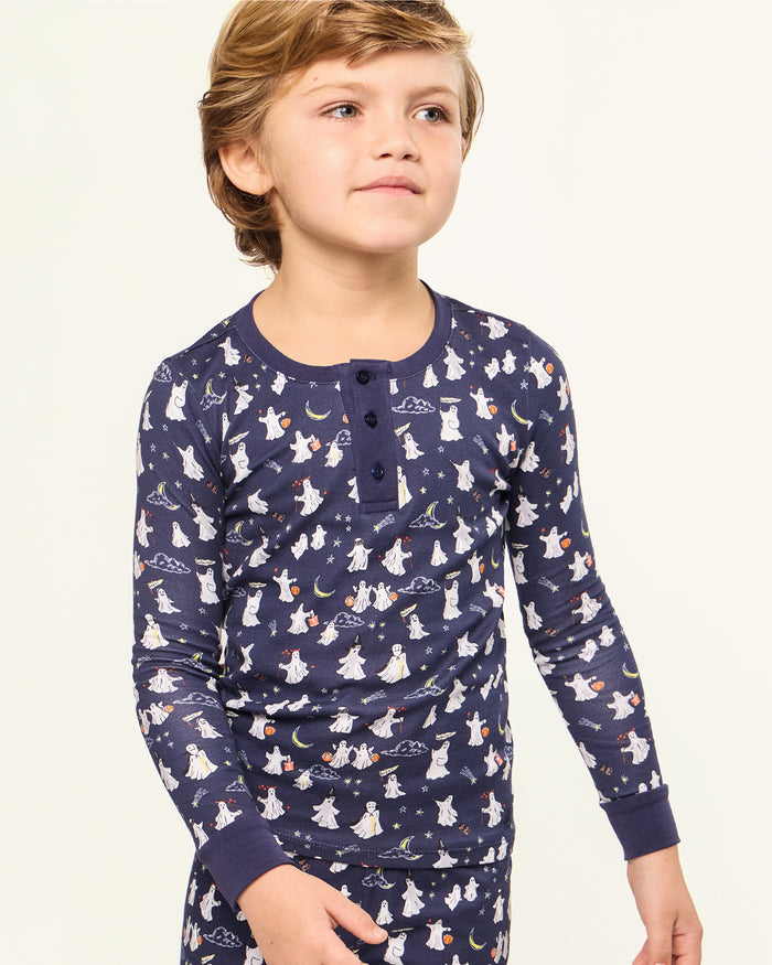 The Kid's Pima Snug Fit Pajama Set in Spooky Slumber is a navy blue pajama set with long sleeves and pants, featuring white and red cartoon dogs in winter gear, plus dark blue cuffs and button details on the top.