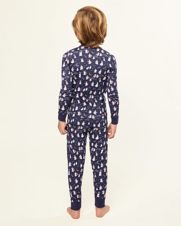 The Kid's Pima Snug Fit Pajama Set in Spooky Slumber is a navy blue pajama set with long sleeves and pants, featuring white and red cartoon dogs in winter gear, plus dark blue cuffs and button details on the top.