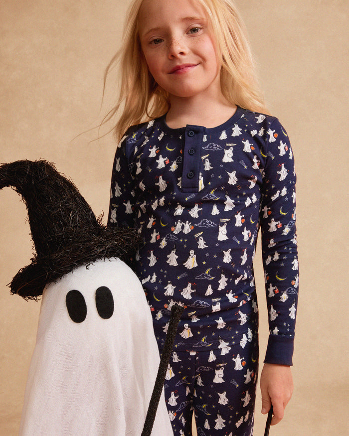 The Kid's Pima Snug Fit Pajama Set in Spooky Slumber is a navy blue pajama set with long sleeves and pants, featuring white and red cartoon dogs in winter gear, plus dark blue cuffs and button details on the top.