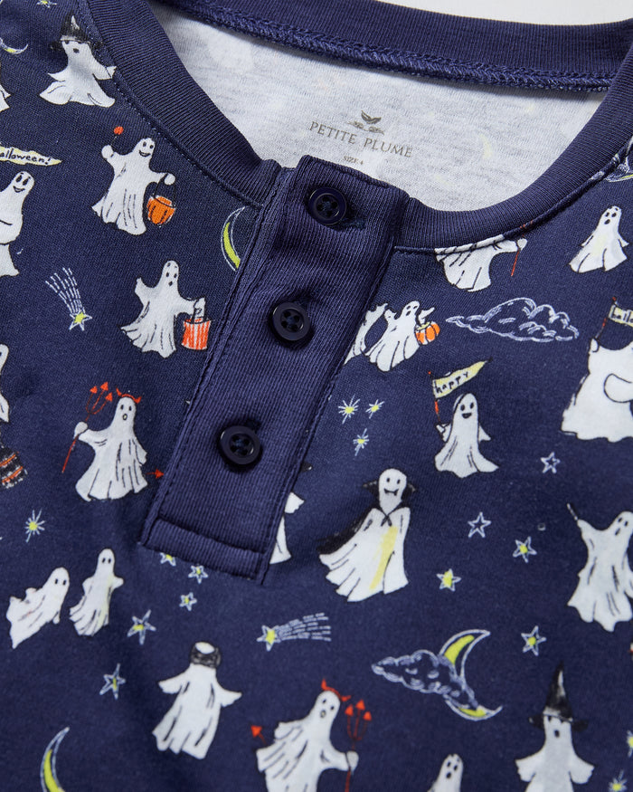 The Kid's Pima Snug Fit Pajama Set in Spooky Slumber is a navy blue pajama set with long sleeves and pants, featuring white and red cartoon dogs in winter gear, plus dark blue cuffs and button details on the top.