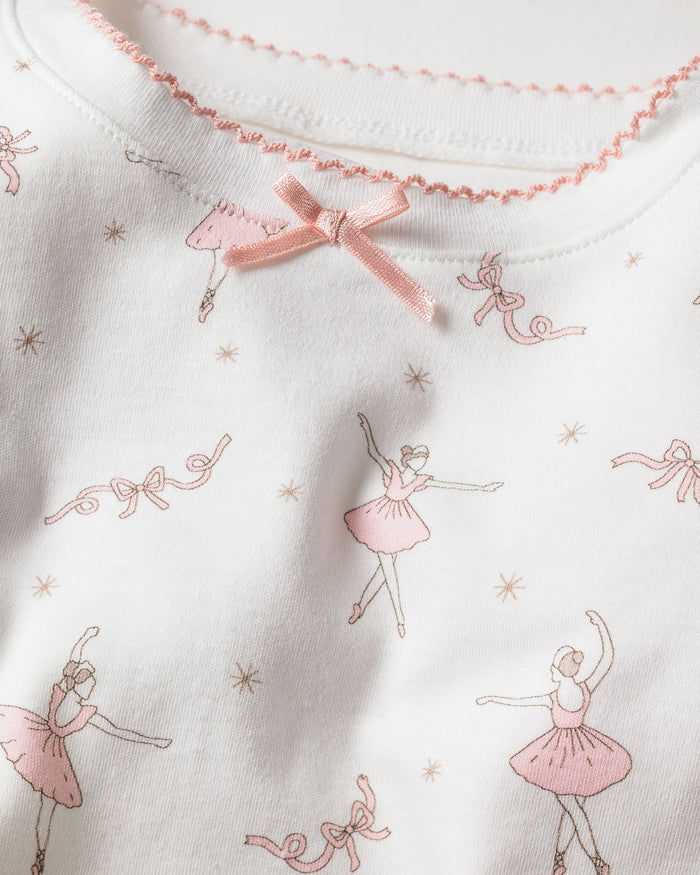 The Kids Pima Snug Fit Pajama Set in Sugar Plum Fairy by Petite Plume features white Pima cotton fabric with pink ballerina, ribbon, and star illustrations. A small pink bow adorns the round neckline of the long sleeve top and pant ensemble, adding a delicate touch.