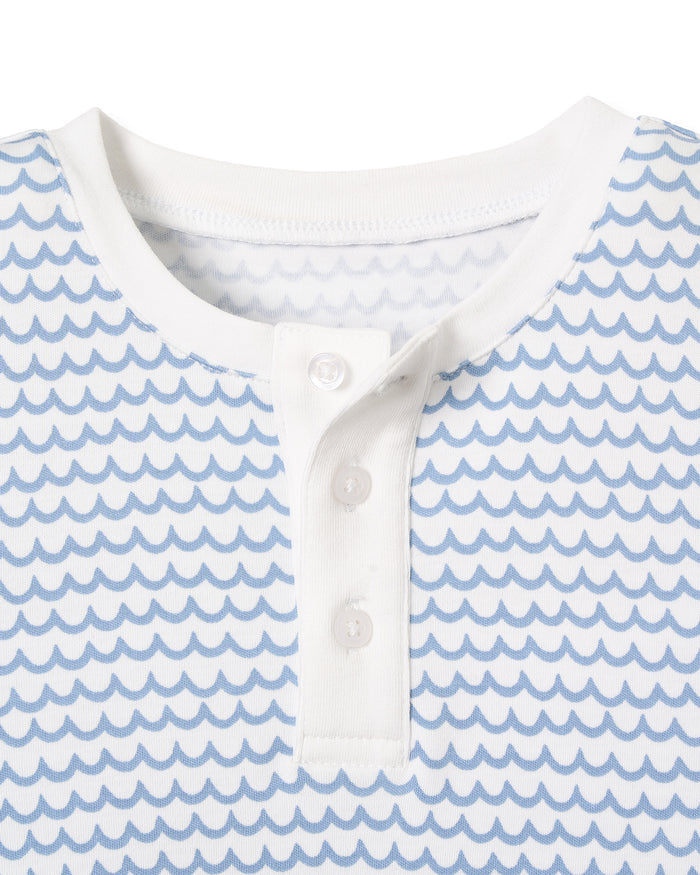 A close-up of Petite Plumes Kids Pima Snug Fit Pajama Short Set in La Mer. The short sleeve top is crafted from soft Pima cotton, with a round neck and three buttons. It features a light blue wave-like pattern on white fabric, ideal for sleepwear, with solid white neckline and button placket.