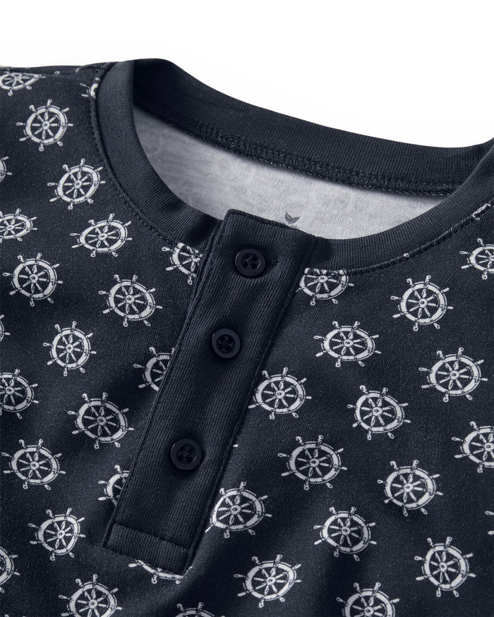 Close-up of the Kid’s Pima Snug Fit Short Set in Captain’s Compass, showcasing a navy blue shirt adorned with a nautical ship wheel pattern, finished with a ribbed collar and a three-button placket.