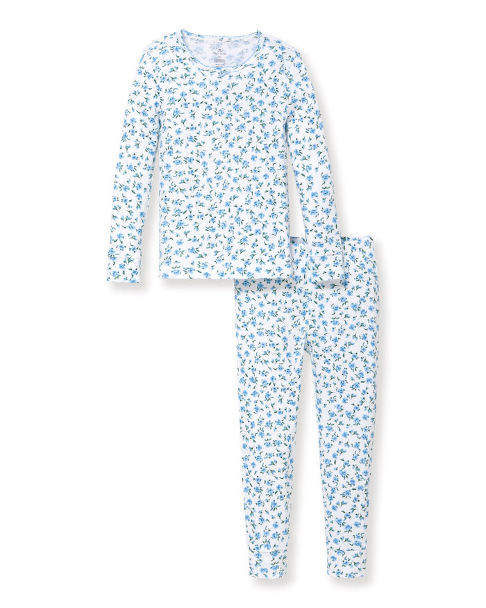 A young child with long curly hair stands barefoot against a plain background, wearing the Kid's Pointelle Snug Fit Pajama Set in Blue Floral.