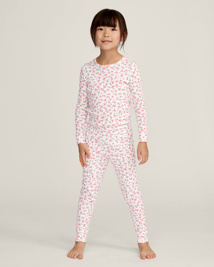 A young girl stands barefoot against a plain background, wearing the Kid's Pointelle Snug Fit Pajama Set in Pink Floral. She faces forward with a relaxed, neutral expression.