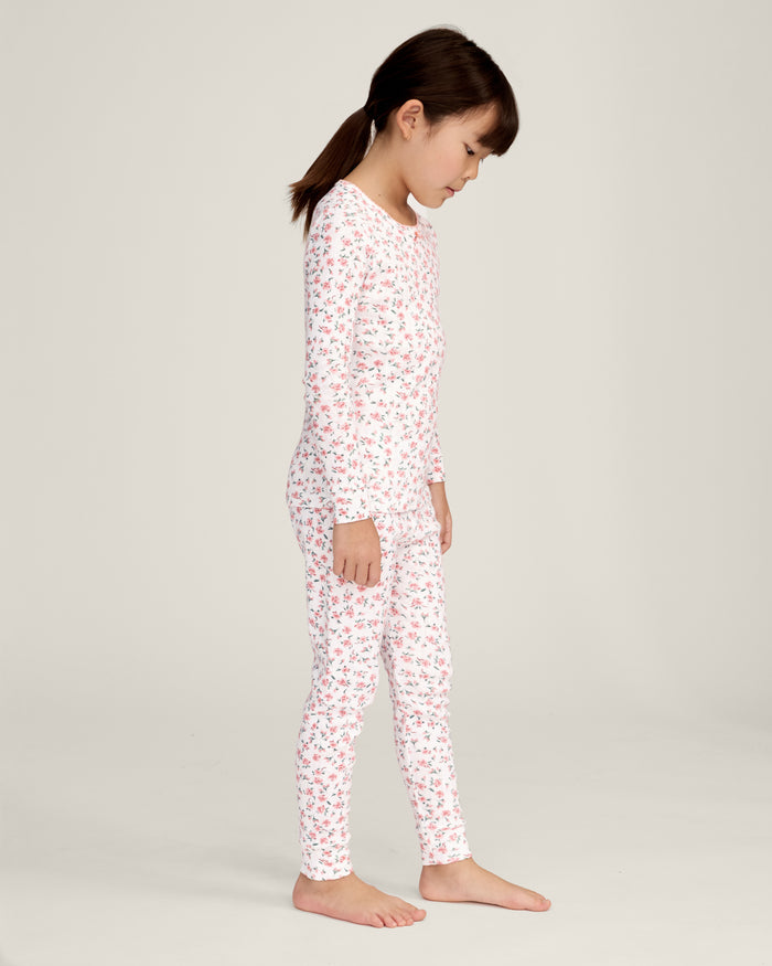 A young girl stands barefoot against a plain background, wearing the Kid's Pointelle Snug Fit Pajama Set in Pink Floral. She faces forward with a relaxed, neutral expression.
