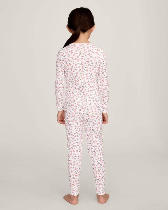 A young girl stands barefoot against a plain background, wearing the Kid's Pointelle Snug Fit Pajama Set in Pink Floral. She faces forward with a relaxed, neutral expression.