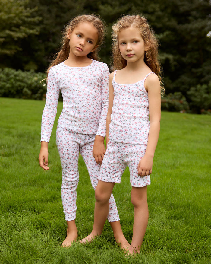 A young girl stands barefoot against a plain background, wearing the Kid's Pointelle Snug Fit Pajama Set in Pink Floral. She faces forward with a relaxed, neutral expression.