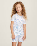 A young girl with long, curly light brown hair stands against a plain background, wearing the Kid's Pointelle Snug Fit Pajama Short Set in Blue Floral. She looks at the camera with a gentle expression.