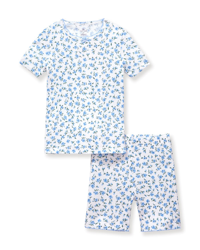 A young girl with long, curly light brown hair stands against a plain background, wearing the Kid's Pointelle Snug Fit Pajama Short Set in Blue Floral. She looks at the camera with a gentle expression.