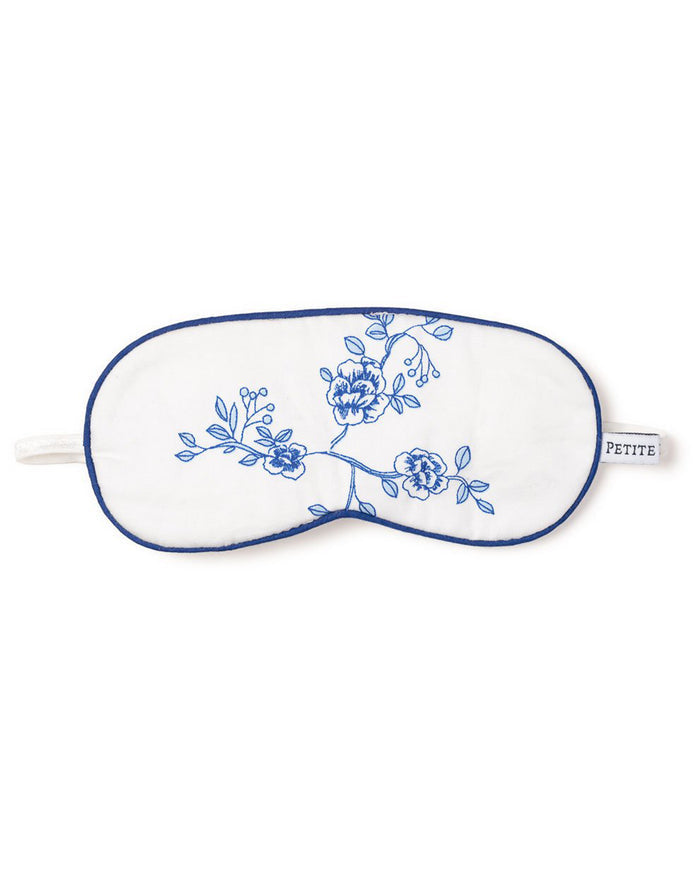 The Kids Sleep Mask in Indigo Floral by Petite Plume features blue floral embroidery with blossoms and leaves, trimmed in blue with an elastic strap. Its small tag reads PETITE PLUME, making it a dreamy, customizable gift.