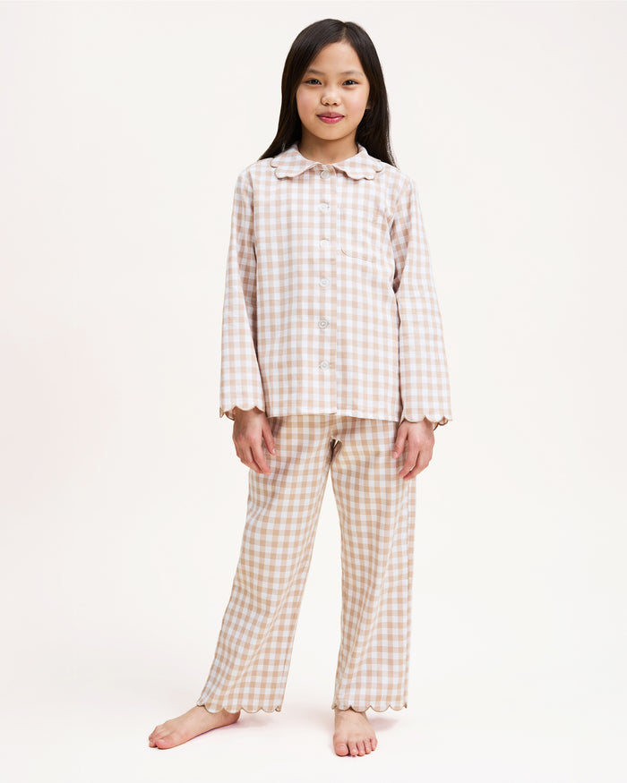 Kid's Twill Colette Pajama Set in Camel Gingham, featuring a beige and white gingham pattern with a scalloped collar, long sleeves, front pocket, and matching elastic-waist pants, is displayed neatly on a white background.