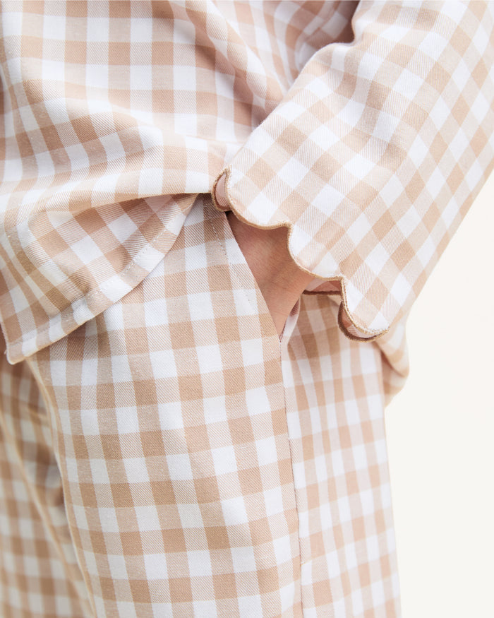 Kid's Twill Colette Pajama Set in Camel Gingham, featuring a beige and white gingham pattern with a scalloped collar, long sleeves, front pocket, and matching elastic-waist pants, is displayed neatly on a white background.