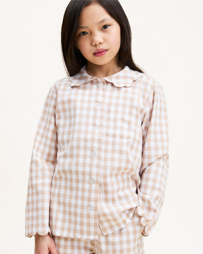 Kid's Twill Colette Pajama Set in Camel Gingham, featuring a beige and white gingham pattern with a scalloped collar, long sleeves, front pocket, and matching elastic-waist pants, is displayed neatly on a white background.