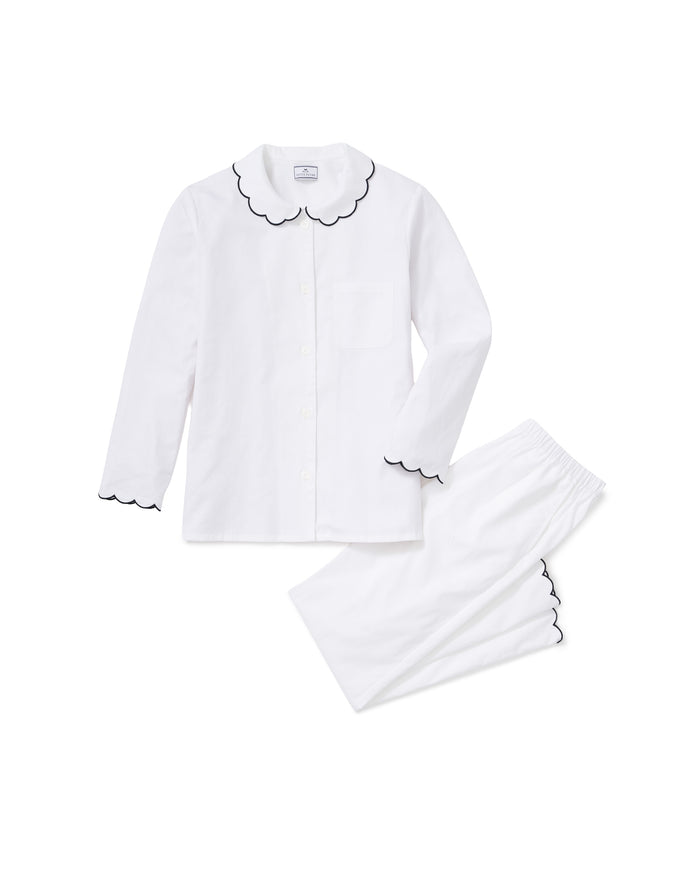 Kid’s Twill Colette Pajama Set in White with Navy Piping: A two-piece pajama set featuring a long-sleeve button-up top with a front pocket and matching pants. Both pieces have scalloped edging accented with navy piping along the collar, cuffs, and pant legs.