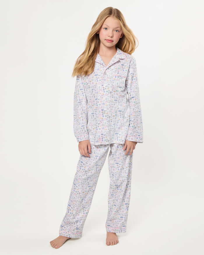 The Kid's Twill Pajama Set in Baking Spirits Bright features white long-sleeve button-up top and long pants with a colorful print of various small household and travel items.
